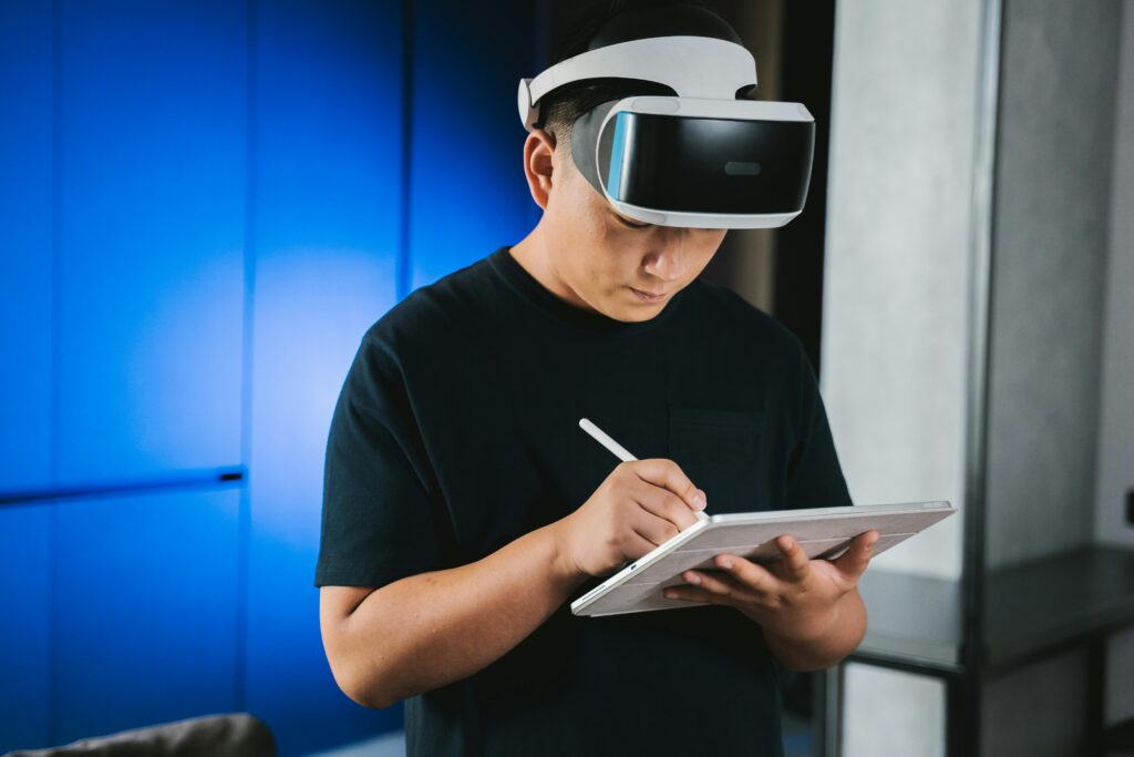 A man indoors wearing a VR headset while writing on a tablet with a stylus pen.